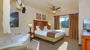 A hotel room with a large bed, a bathtub, a ceiling fan, and a TV. - Ridge Pointe (Stateline)