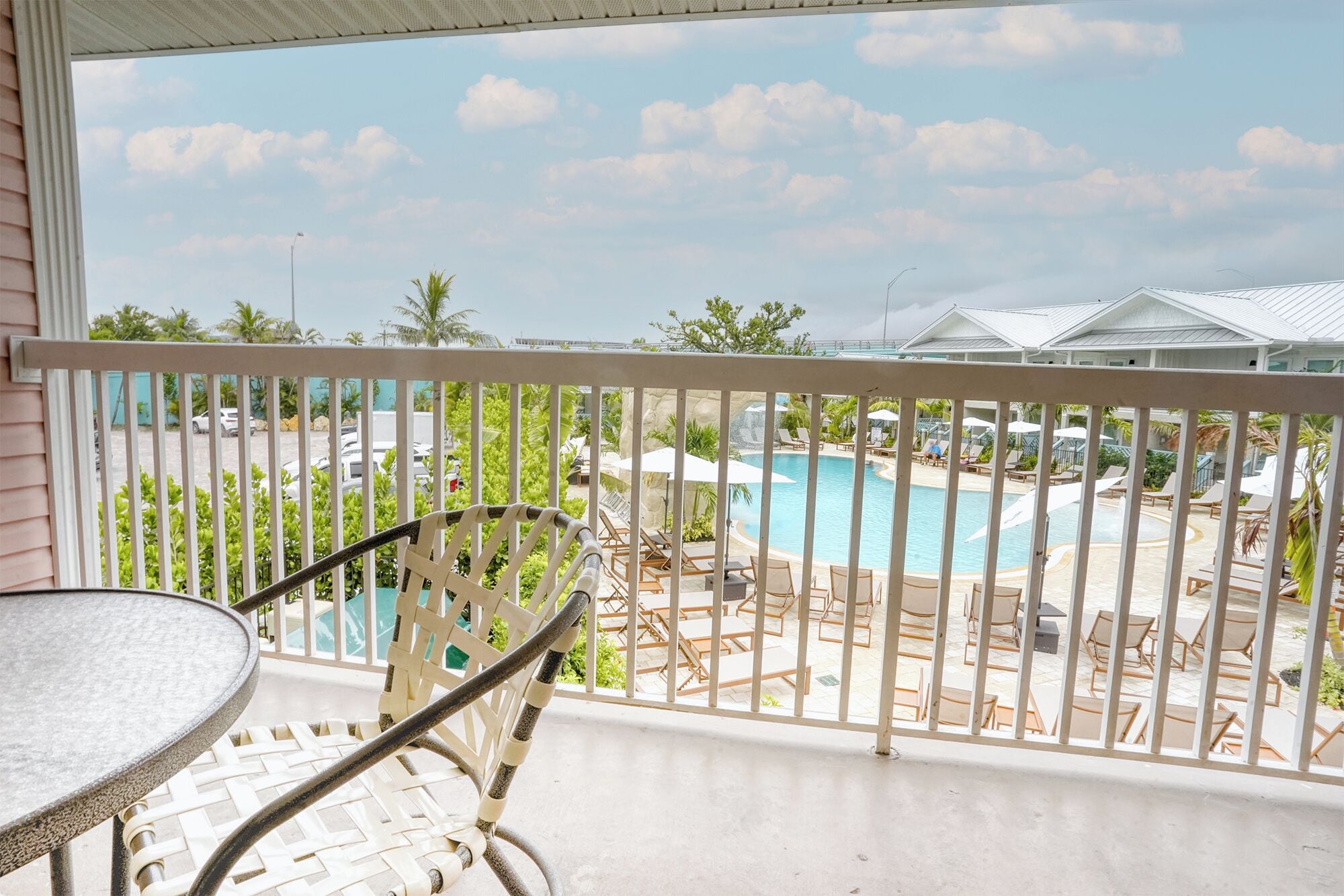 A balcony with a view of a swimming pool, lounge chairs, and a tropical setting.