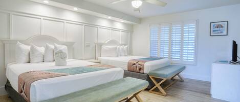 A hotel room with two beds, a ceiling fan, and a desk with a computer.