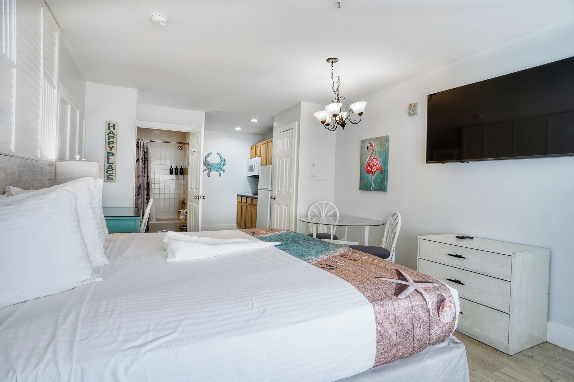 A bedroom with a bed, a desk, a chair, a TV, and a bathroom visible in the background.