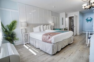A bedroom with a large bed, a bedside table, a lamp, a potted plant, and a wall-mounted shelf.