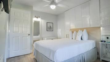 A bedroom with a bed, a ceiling fan, a bedside table with a clock, and a mirror.