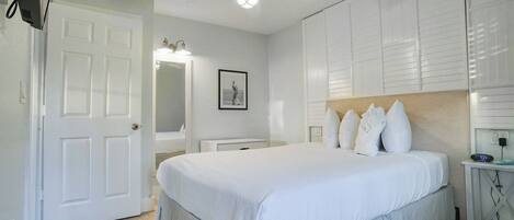 A bedroom with a bed, a ceiling fan, a bedside table with a clock, and a mirror.
