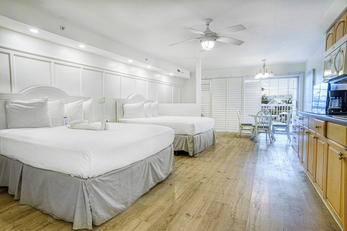 A hotel room with two beds, a kitchenette, and a dining area with a view.