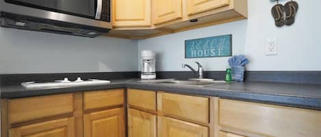 A kitchen with wooden cabinets, a stainless steel microwave, a coffee maker, and a sink.