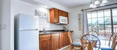 A kitchen with wooden cabinets, a white refrigerator, a microwave, and a dining area with wicker chairs.