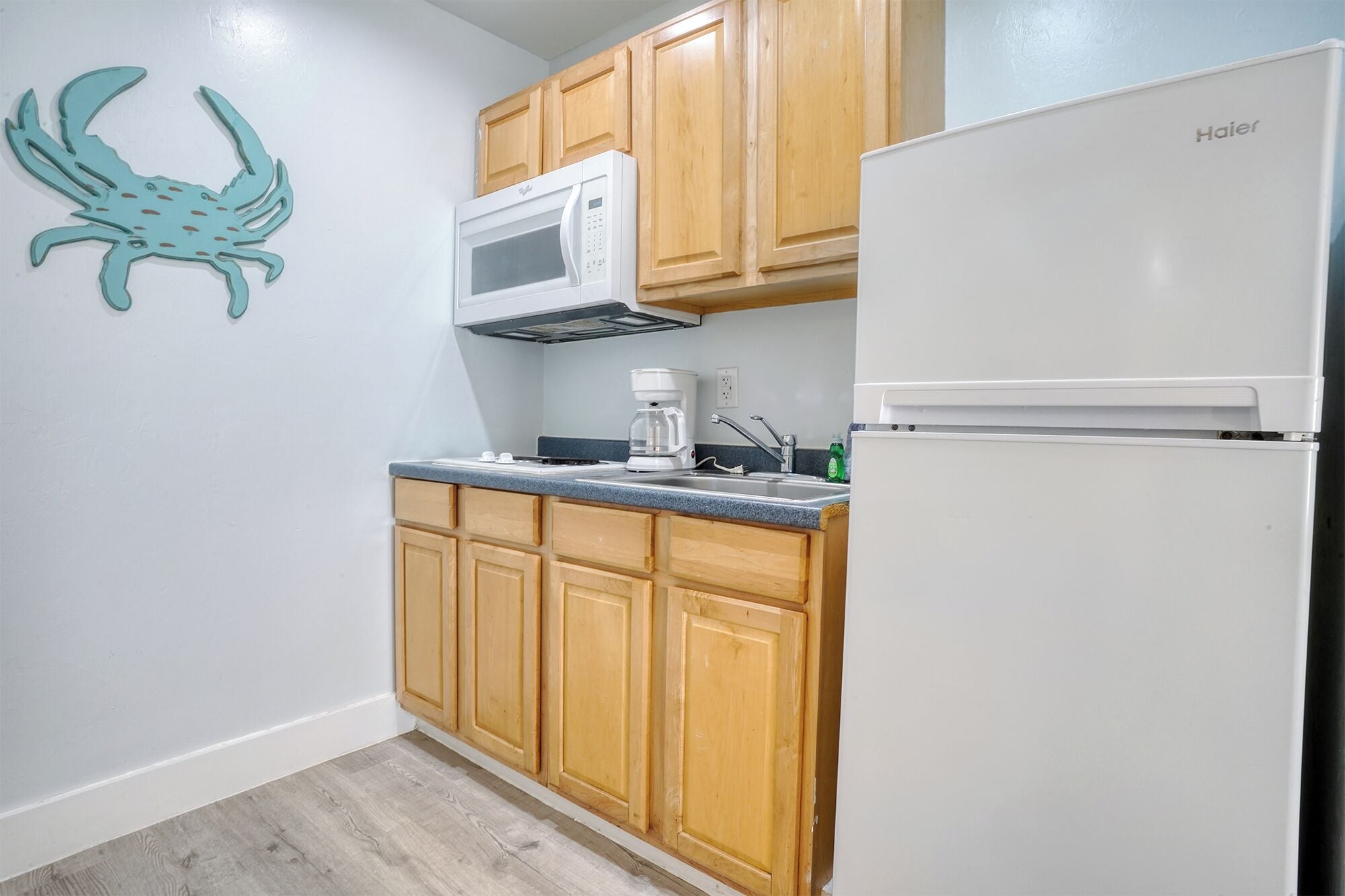 A compact kitchen with wooden cabinets, a white refrigerator, a microwave, and a coffee maker.