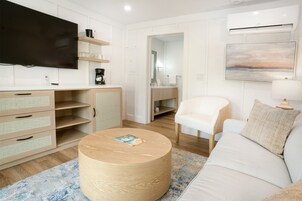 A modern living room with a flat-screen TV, wooden furniture, a round coffee table, a white sofa, and a painting on the wall.