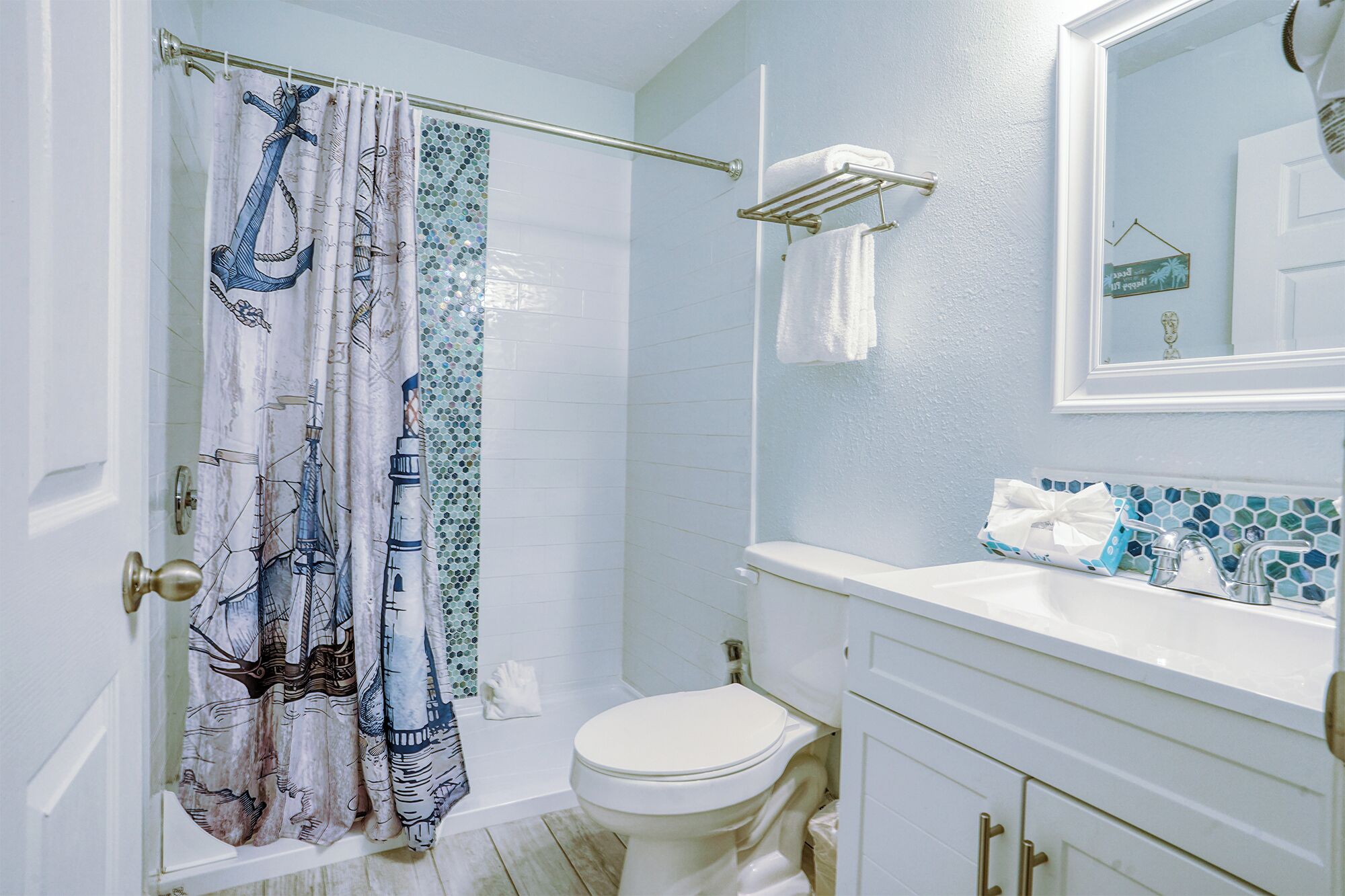 Une salle de bain équipée d’un rideau de douche orné de motifs marins, de toilettes, d’un lavabo avec un miroir au-dessus et d’un porte-serviettes.