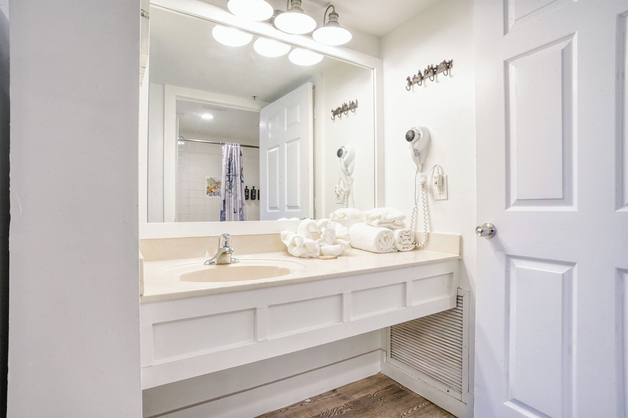 Une salle de bain avec un double vasque, un grand miroir et deux sèche-cheveux fixés au mur.
