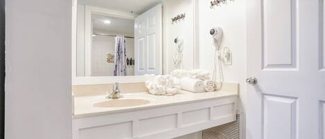 Une salle de bain avec un double vasque, un grand miroir et deux sèche-cheveux fixés au mur.