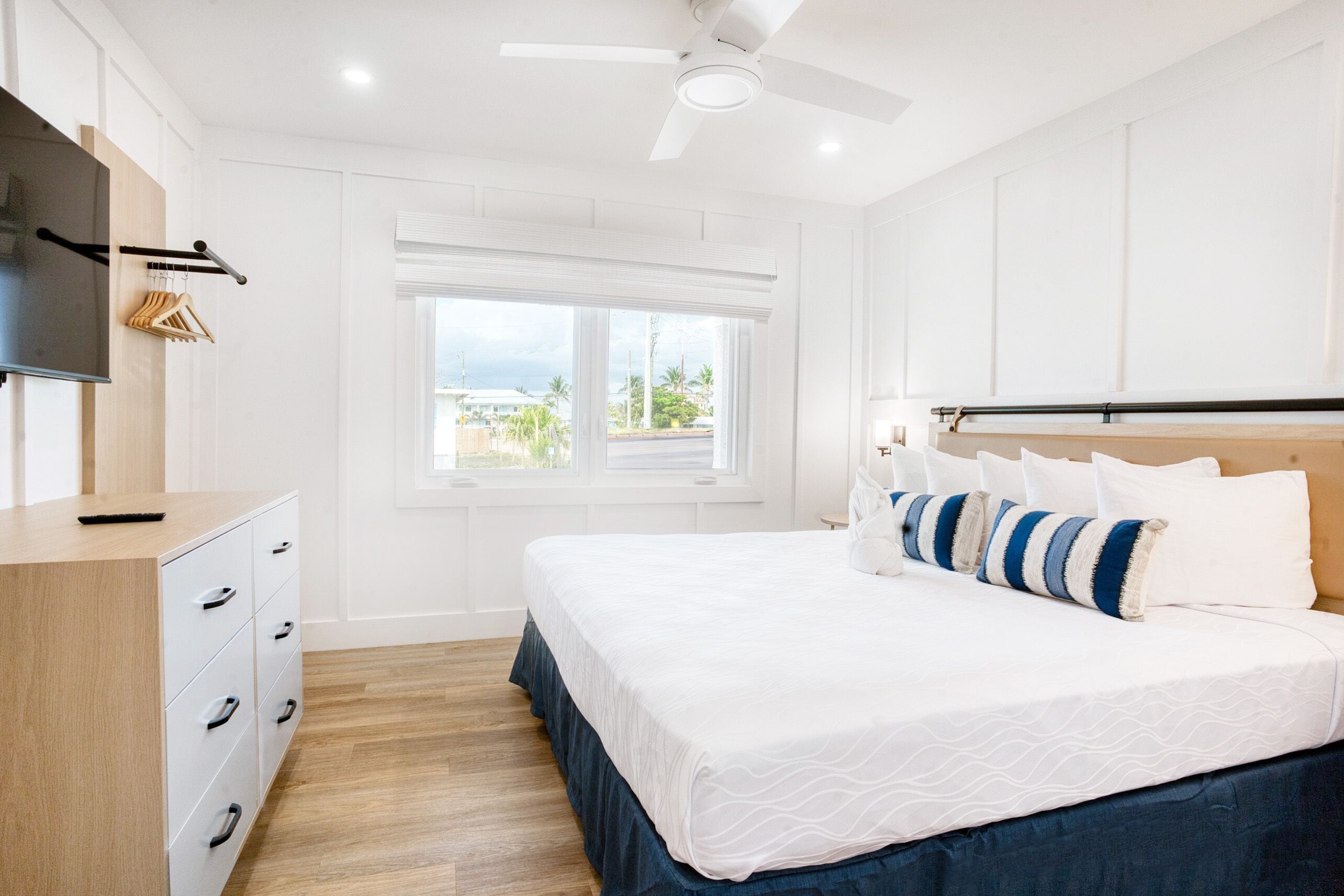 A bedroom with a bed, a dresser, a TV, and a window with a view.