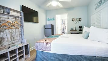 Un dormitorio con cama, ventilador de techo, televisión, refrigerador y un letrero en la pared que dice 'Beach House'.