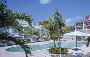 A pool area with lounge chairs, umbrellas, and palm trees. - The Lighthouse Resort Inn & Suites (Fort Myers Beach)