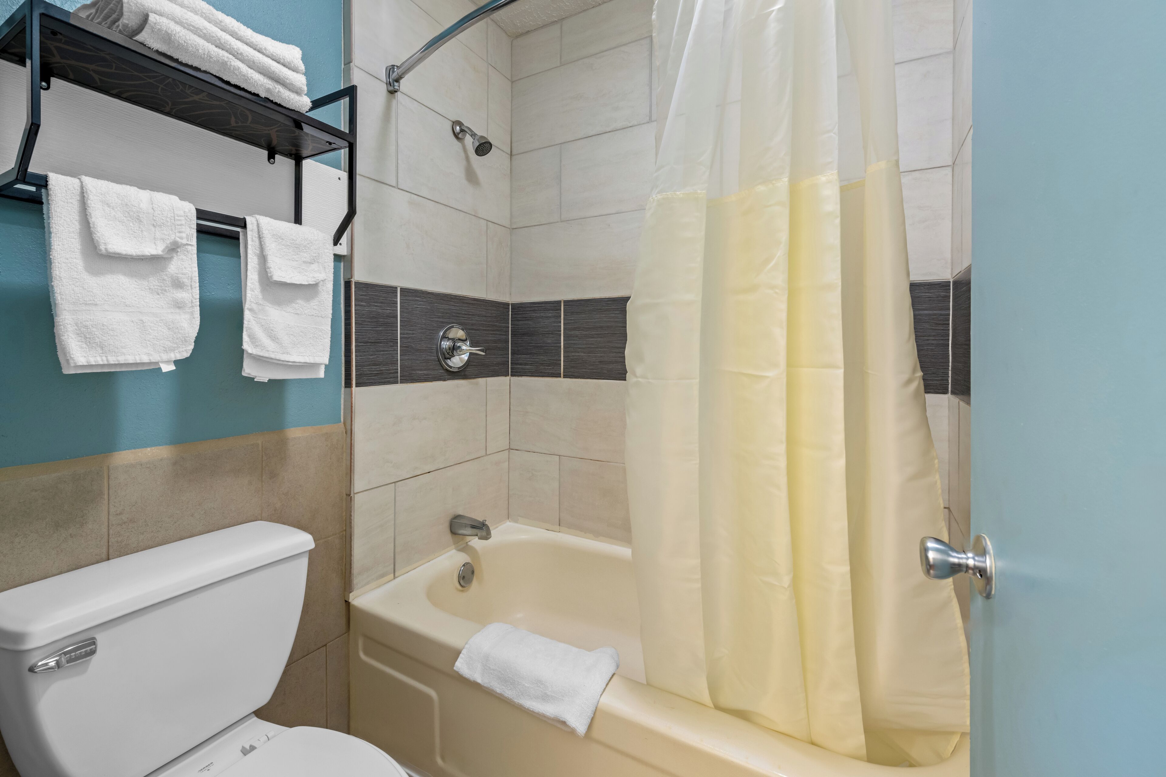 A bathroom with a toilet, bathtub, shower curtain, and towel rack.