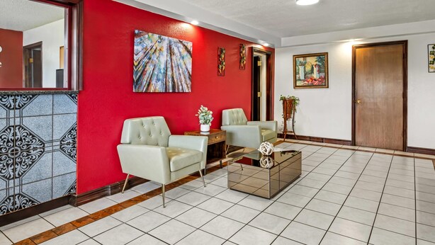A hotel lobby with a red accent wall, two light-colored armchairs, a glass coffee table, and a wooden door. - Econo Lodge Charlotte Airport Area (Charlotte)