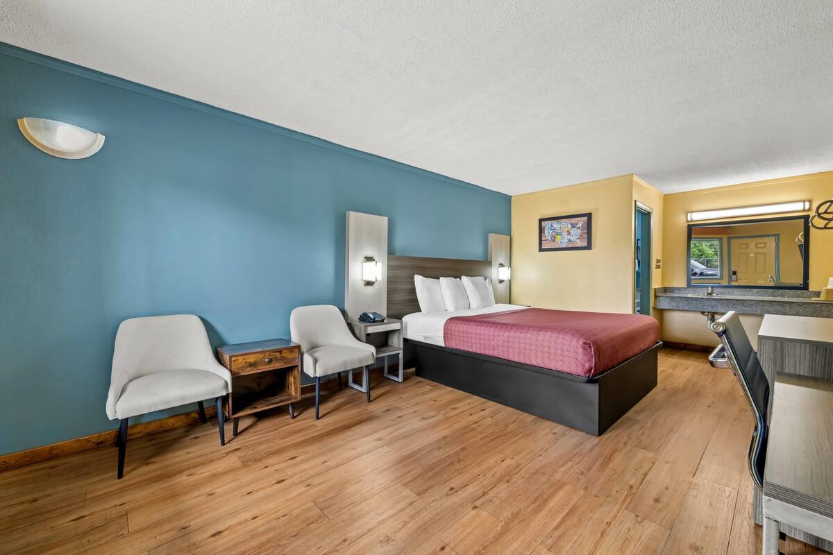 Ein Hotelzimmer mit einem Bett, zwei Stühlen, einem Schreibtisch und einem Spiegel.