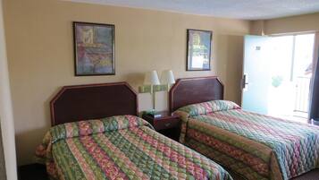 A hotel room with two beds, a nightstand, a lamp, and two framed pictures on the wall.