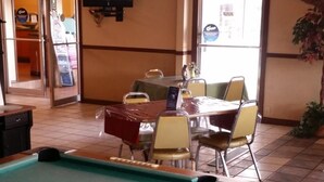 A pool table in a room with a wooden ceiling, a dining area with chairs, and a television mounted on the wall. - Red Carpet Inn (Hot Springs)