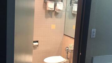 A bathroom with a toilet, a towel rack with towels, a mirror, and a tiled floor.