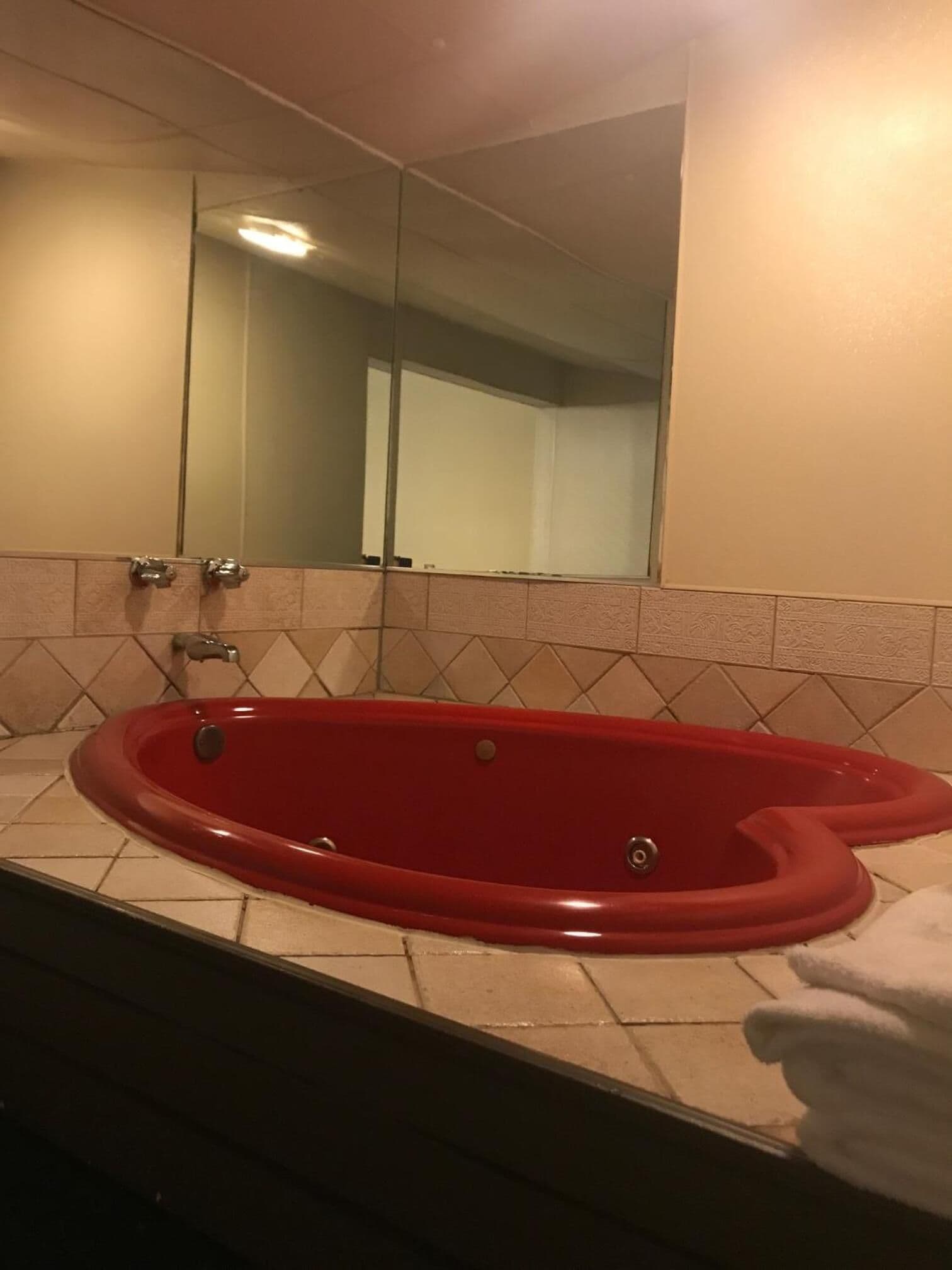 Een rood bad met een spiegel erboven, een handdoek ernaast en een betegelde vloer.