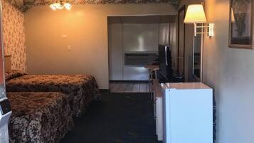 Habitación de hotel con dos camas, ventilador de techo, kitchenette y refrigerador pequeño.