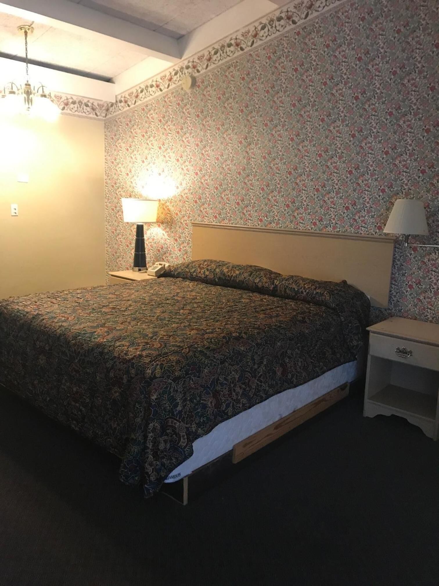 A bedroom with a bed, two bedside tables, a lamp, and a floral-patterned wall.