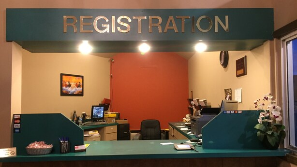 A registration desk with a sign above it, a computer, a chair, and a desk with various items on it. - Red Carpet Inn (Hot Springs)