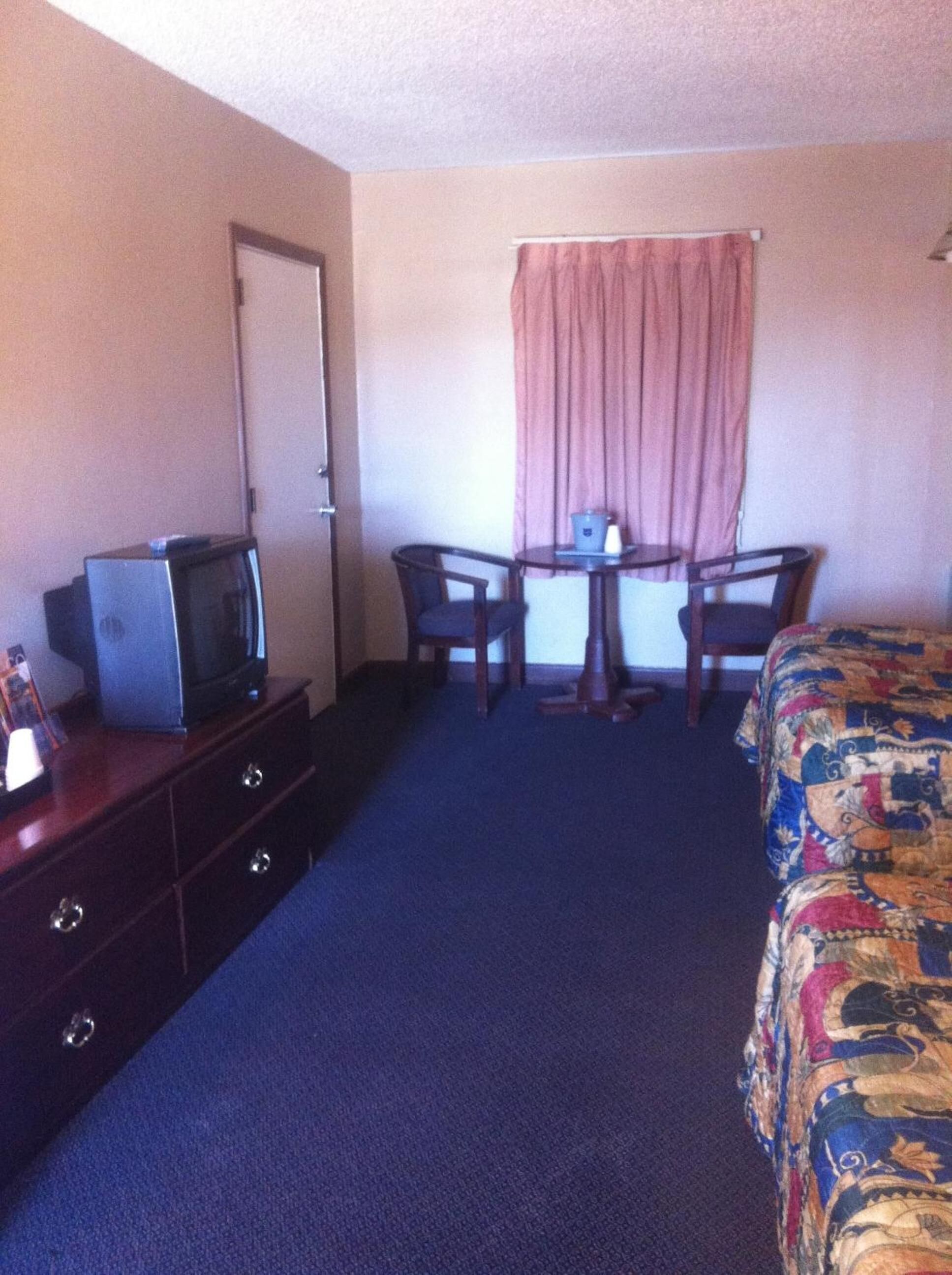Une chambre d’hôtel avec un lit, un bureau avec deux chaises, un téléviseur posé sur une commode et une porte.