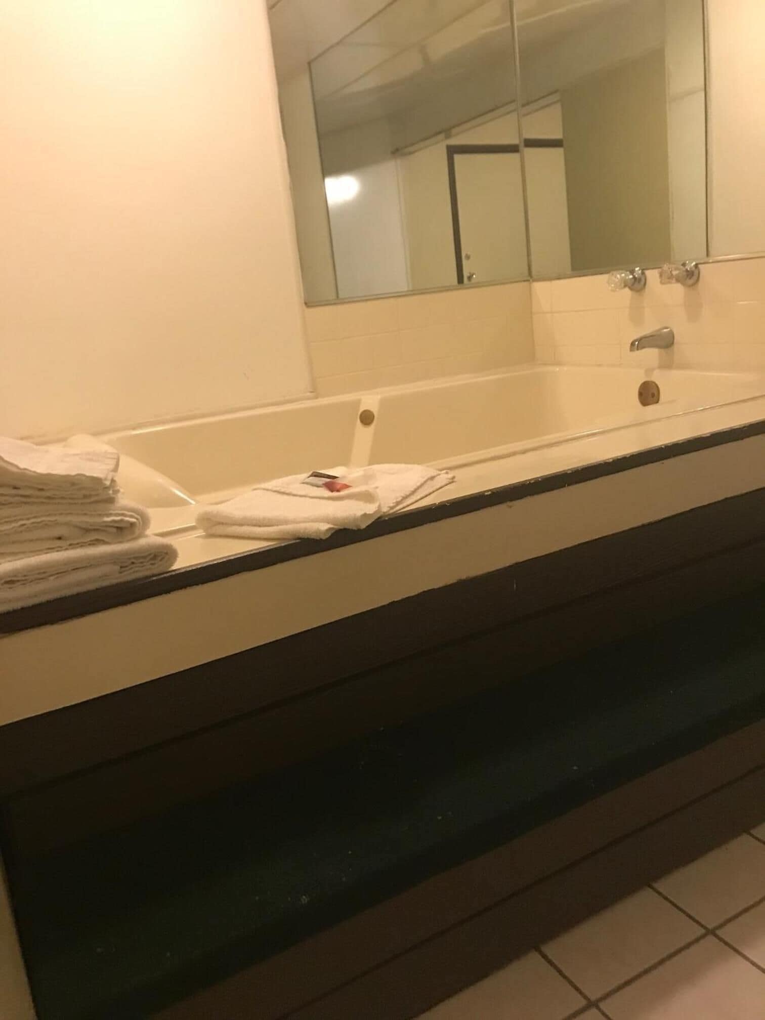 Ein Badezimmer mit einer weißen Badewanne, einem Spiegel darüber und einem Handtuchhalter mit gefalteten Handtüchern.