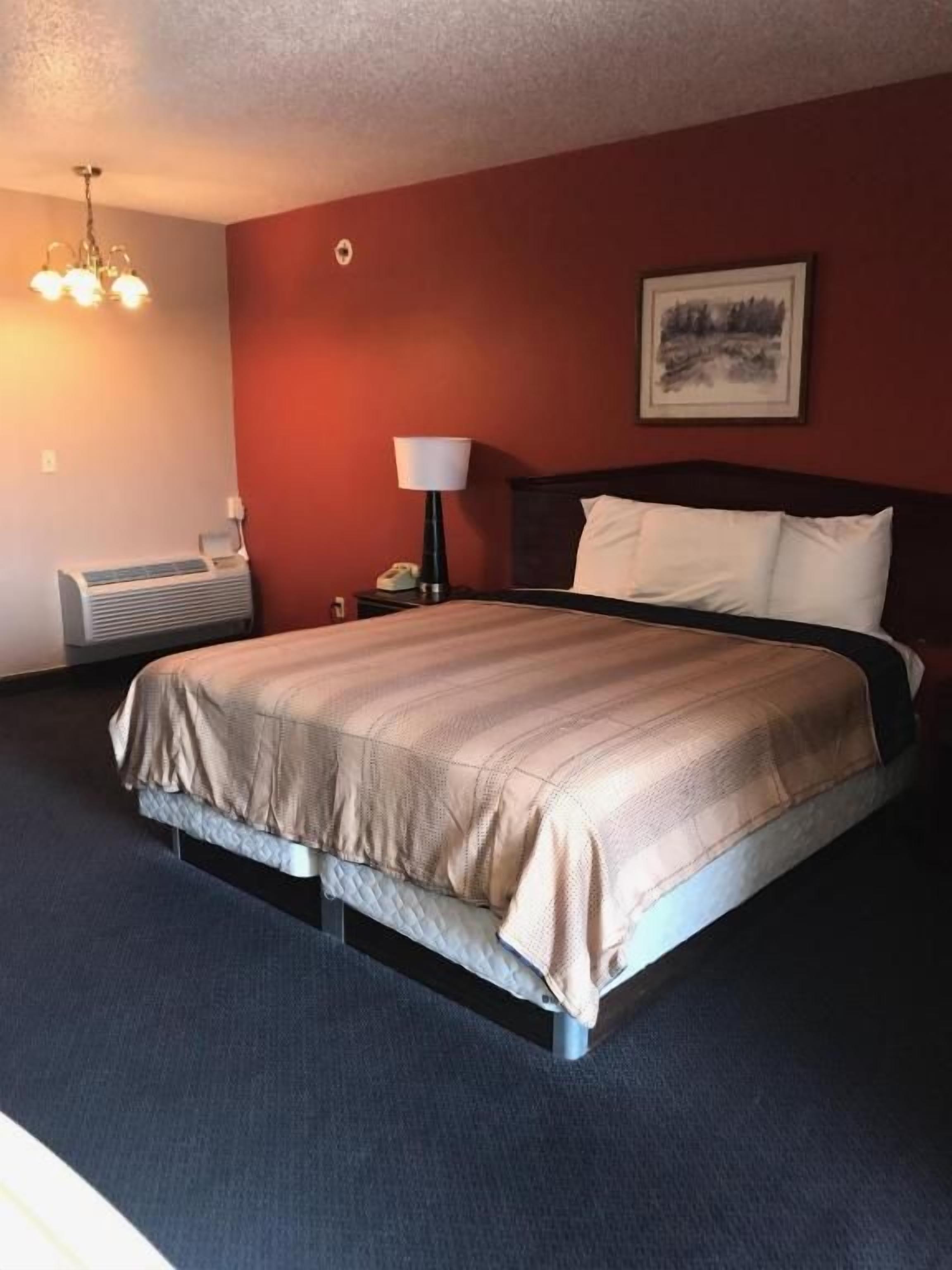 A hotel room with a bed, a nightstand, a lamp, and a painting on the wall.