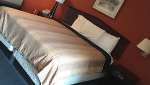 A neatly made bed with a quilted cover, a bedside lamp, and a framed picture on the wall. - Red Carpet Inn (Hot Springs)