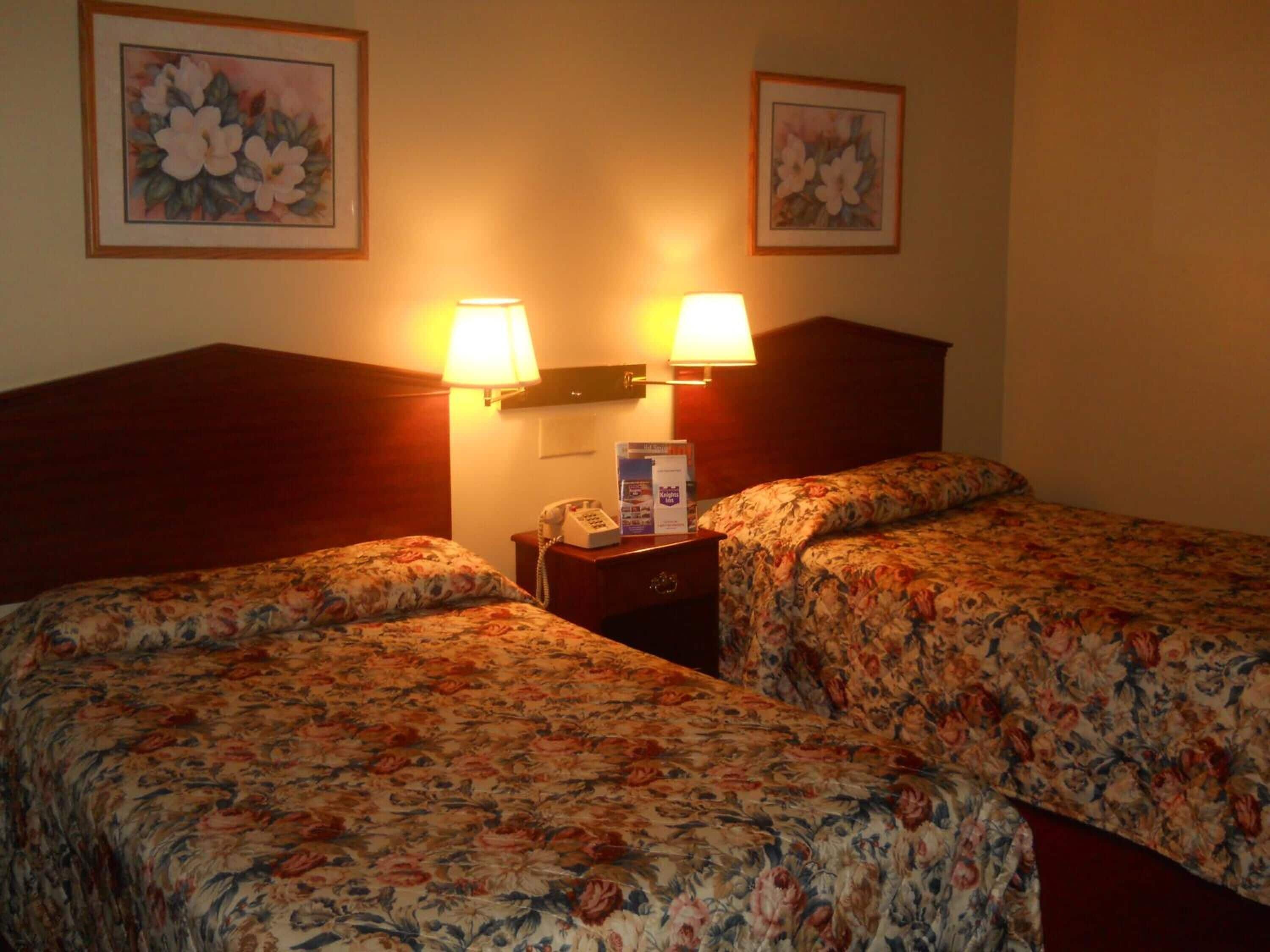 Habitación de hotel con dos camas, cada una con ropa de cama floral, una mesita de noche con lámpara y teléfono.