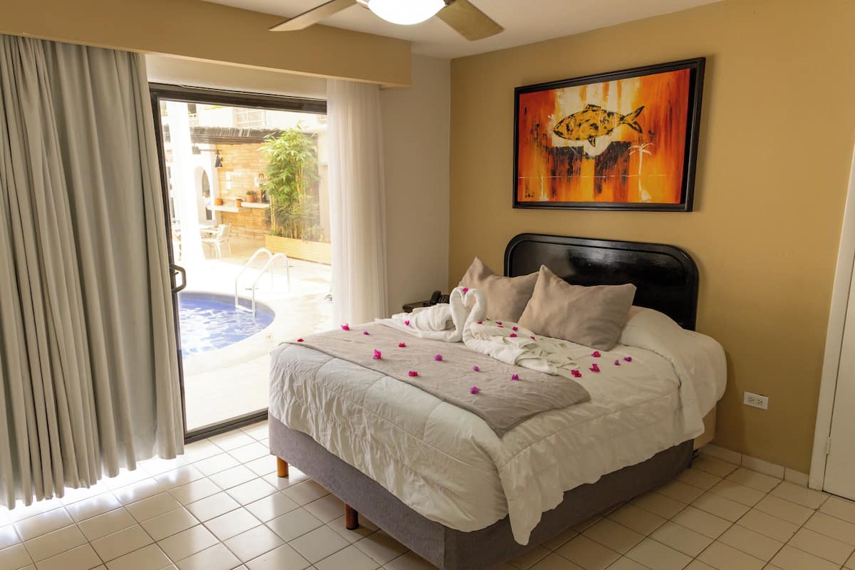 A hotel room with a bed, a painting, and a view through a sliding door.