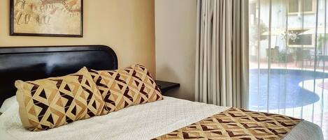 Een hotelkamer met een bed, een schilderij aan de muur en uitzicht op een zwembad.