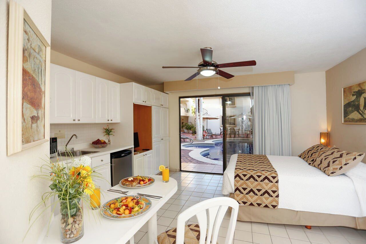 A hotel room with a bed, a desk with breakfast, a view of a swimming pool, and a ceiling fan.