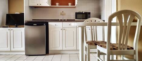 Cocina con armarios blancos, refrigerador de acero inoxidable, microondas y una mesa de comedor con una silla.