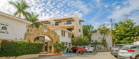 A hotel entrance with a stone archway, paved parking, and a clear blue sky.