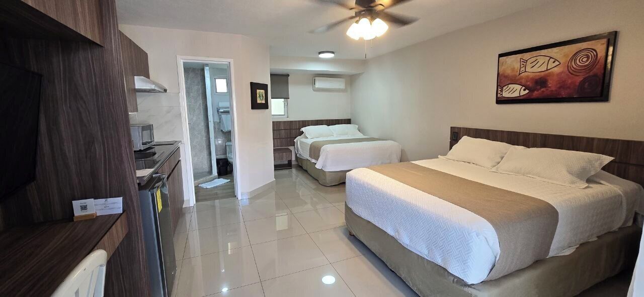 A hotel room with a large bed, a desk, a chair, a ceiling fan, and a painting on the wall.