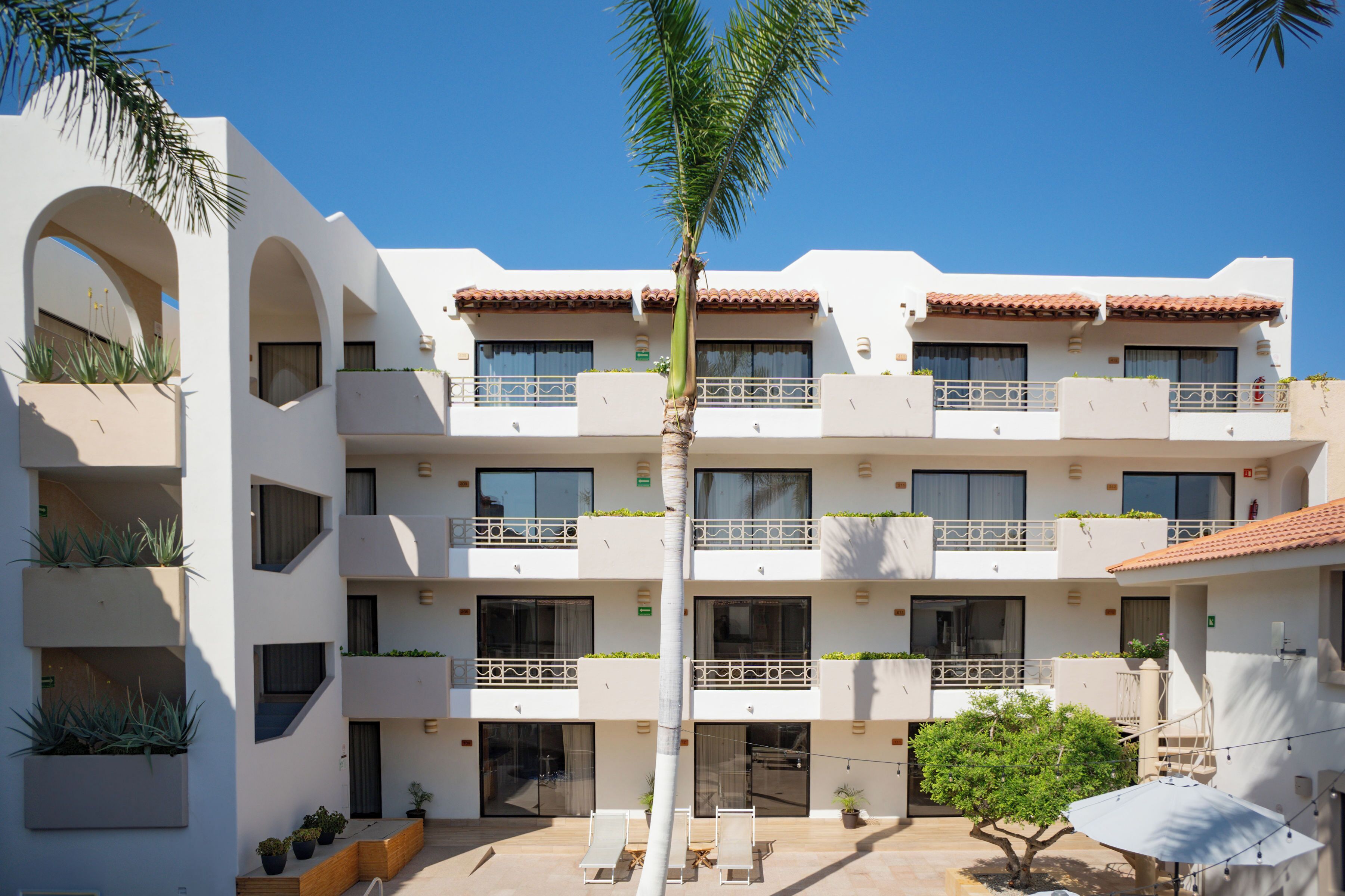 A multi-story hotel with balconies, outdoor seating, and potted plants.