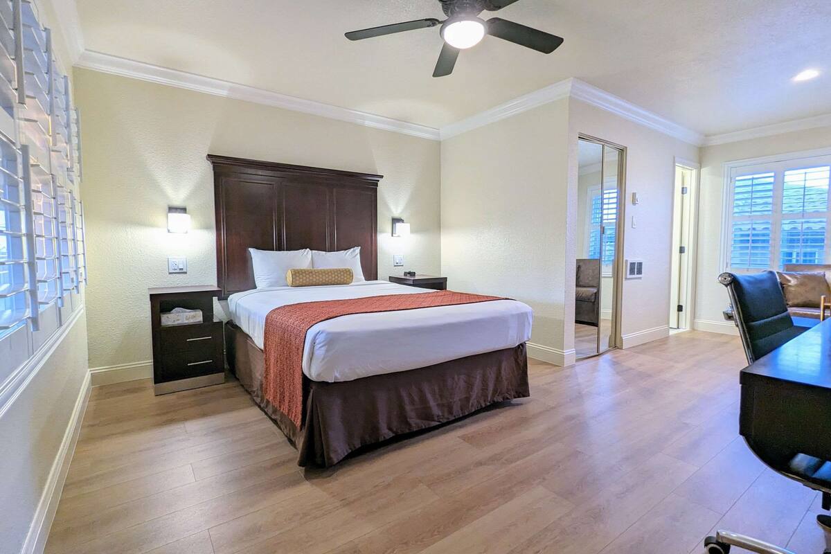Quarto de hotel com cama, mesas de cabeceira, escrivaninha e ventoinha no teto.