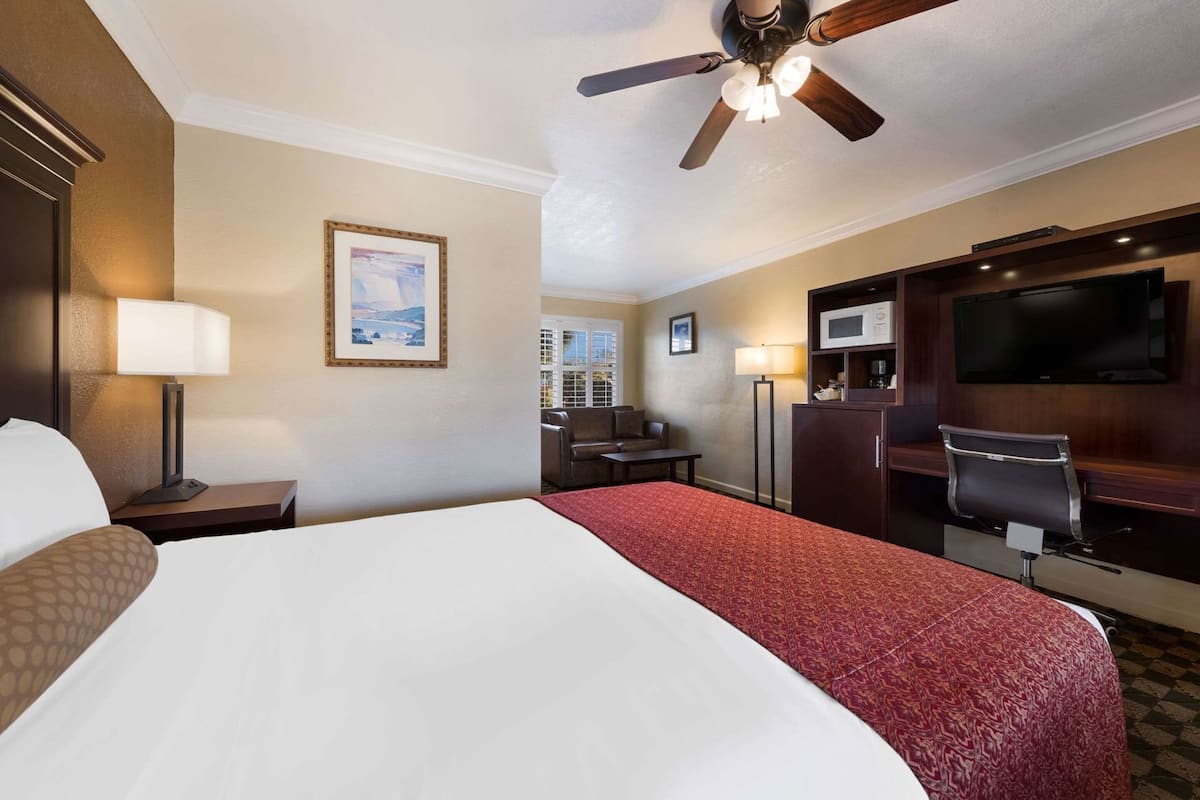 Quarto de hotel com uma cama grande, uma mesa com cadeira, televisão, micro-ondas e ventoinha no teto.