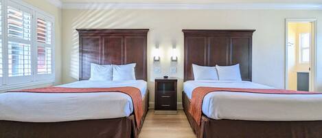 Habitación de hotel con dos camas, un ventilador de techo, una mesita de noche y una ventana con persianas.