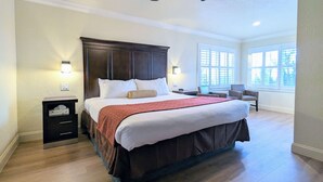 A spacious bedroom with a large bed, a nightstand, a chair, and a window with blinds. - Clarion Collection Wilkie's Inn Pacific Grove - Monterey (Pacific Grove)