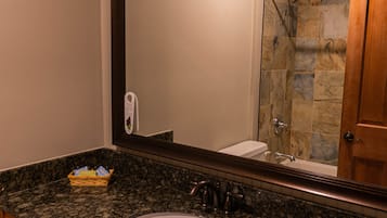 A bathroom with a granite countertop, a sink, a mirror, a shower with stone tiles, and a wooden door.