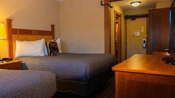 Ein Hotelzimmer mit zwei Betten, einem hölzernen Kopfteil, einem Nachttisch mit Lampe sowie einem Schreibtisch mit Spiegel.