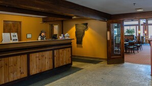 A reception desk with a wooden finish, a small plant, and a seating area with tables and chairs. - The Black Bear Lodge at Stratton Mountain Resort (Stratton)