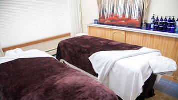Two beds with purple blankets and white linens, a wooden cabinet, and a large window with blinds.