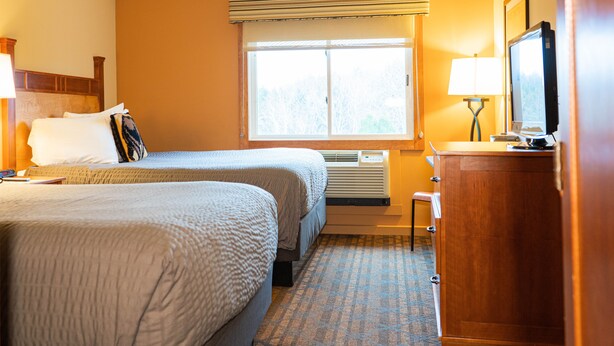 A hotel room with two beds, a window with blinds, a desk with a television, and a lamp. - The Black Bear Lodge at Stratton Mountain Resort (Stratton)