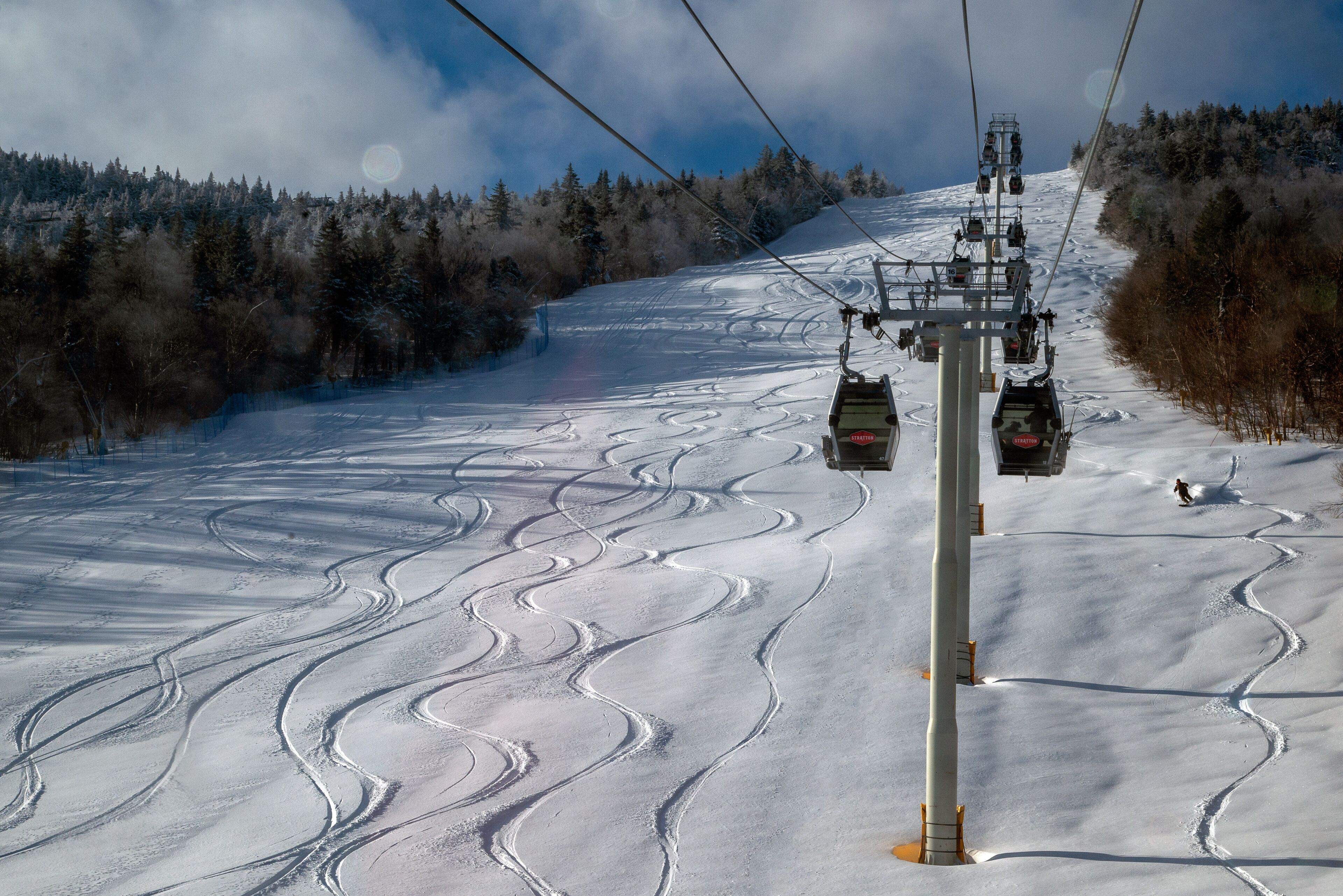 A ski lift chair moving along a snowy slope with tracks.